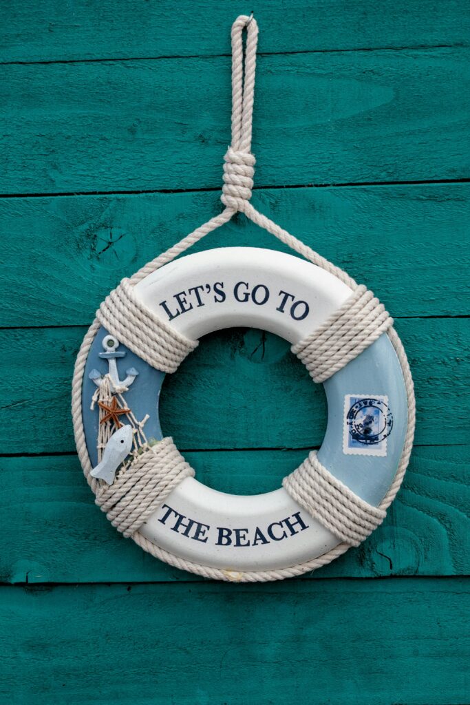 A nautical themed lifebuoy decor with 'Let's Go To The Beach' text hanging on a teal wooden wall.